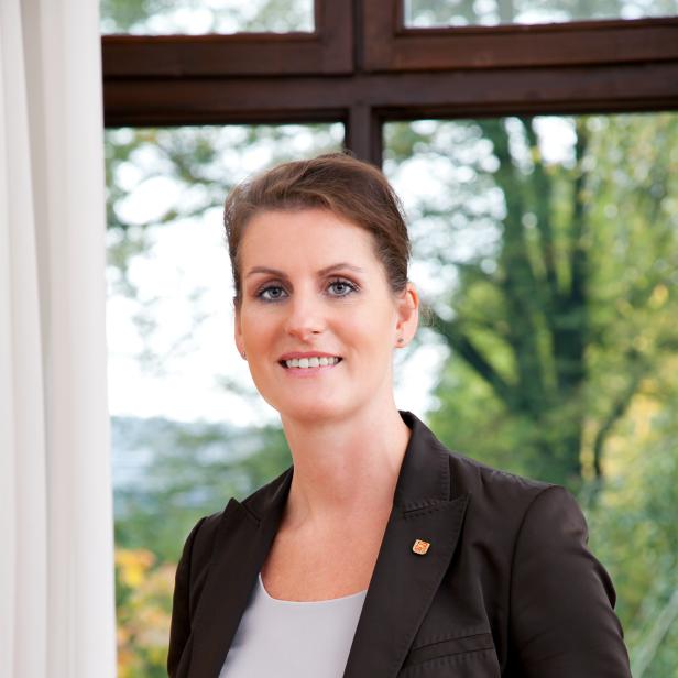 Eine Frau mit Blazer lächelt vor einem Fenster.