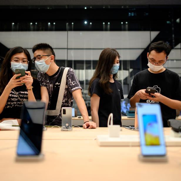 Personen mit Gesichtsmasken betrachten und testen Smartphones in einem Geschäft.