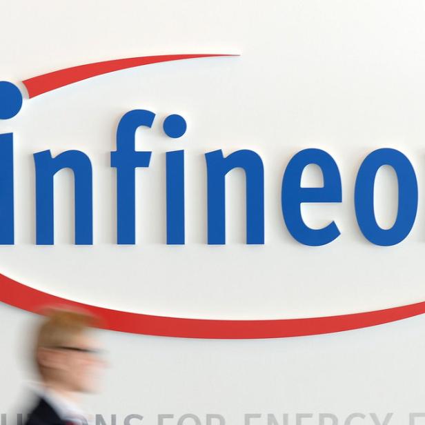 Das blaue Infineon-Logo mit rotem Bogen an einer weißen Wand.