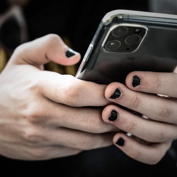 Eine Person hält ein Smartphone in den Händen, die Fingernägel sind schwarz lackiert.