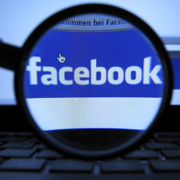 Das Facebook-Logo wird durch eine Lupe betrachtet.