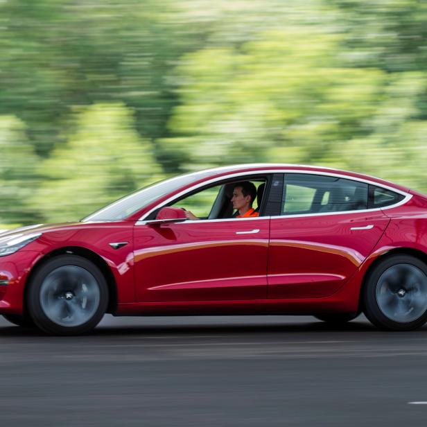 Ein rotes Tesla Model 3 fährt auf einer Straße.