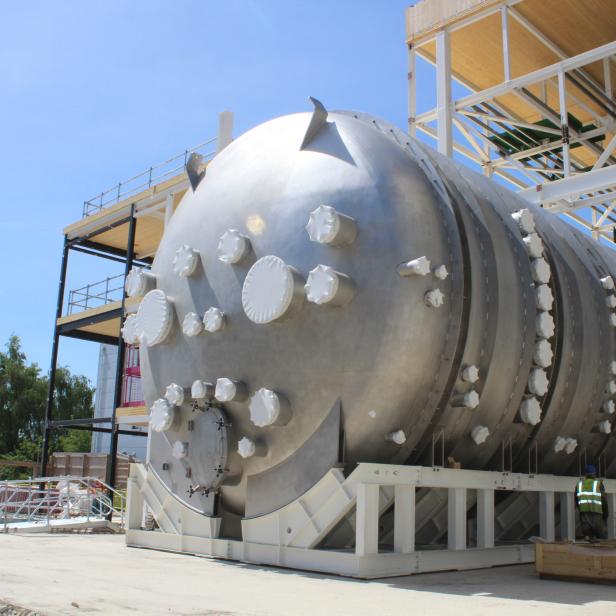 Ein großer, silberner Tank steht auf einer Baustelle unter blauem Himmel.