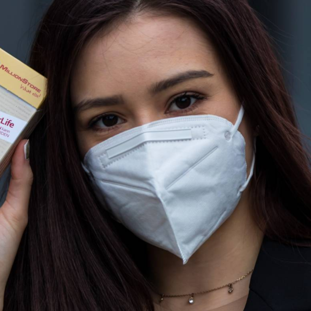 Eine Frau mit Maske hält eine Packung mit der Aufschrift „#SafeYourLife“ in der Hand.
