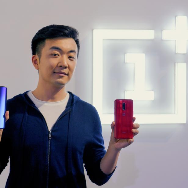 Ein Mann präsentiert ein blaues und ein rotes Smartphone der Marke OnePlus.