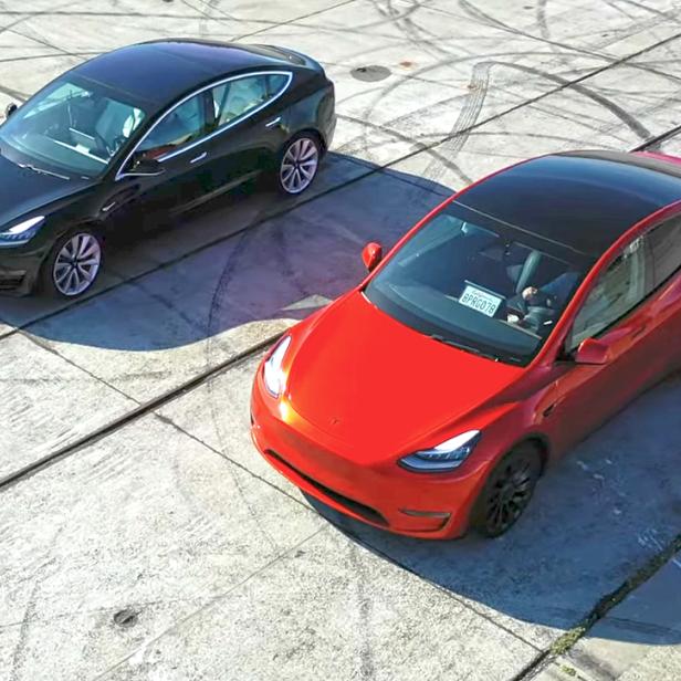 Ein roter und ein schwarzer Tesla stehen auf einem Betonplatz mit Reifenspuren.