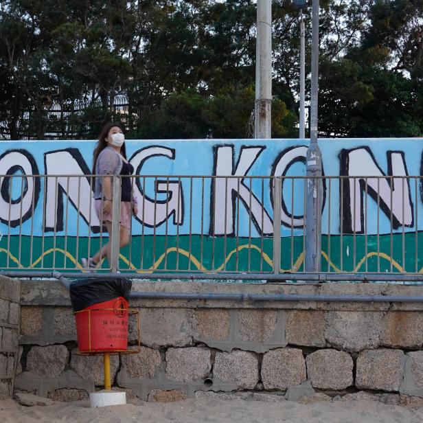 Woman wearing a face mask walks past a graffiti reading "Hong Kong" on a beach at Cheung Chau island during Easter weekend, amid the novel coronavirus disease (COVID-19) outbreak