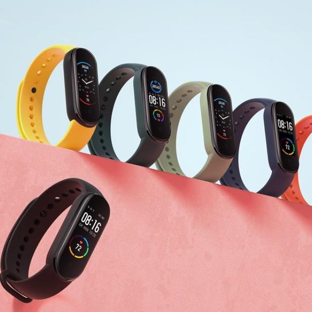 Mehrere Smartwatches mit farbigen Armbändern sind auf einem rosa Untergrund angeordnet.