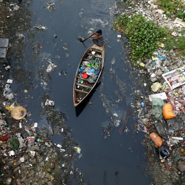 FILE PHOTO: A man on a boat collects plastic materials from dirty water in Dhaka