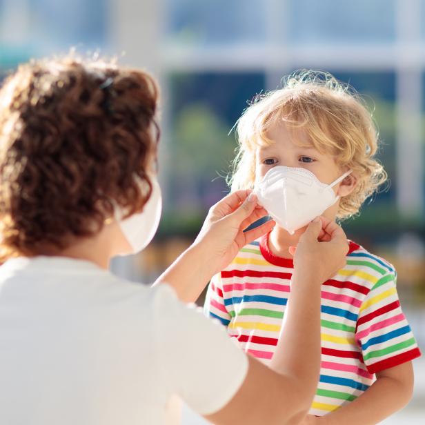 Eine Frau setzt einem kleinen Jungen eine weiße Gesichtsmaske auf.