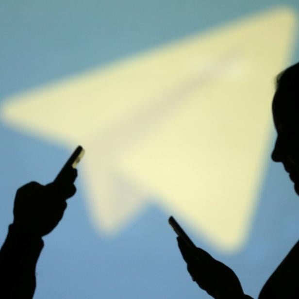 Silhouettes of mobile users are seen next to a screen projection of Telegram logo in this picture illustration