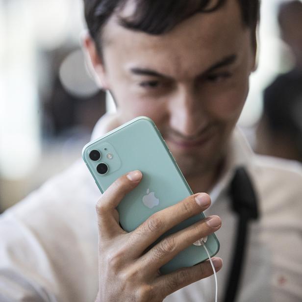 Ein Mann betrachtet ein hellgrünes iPhone in seiner Hand.