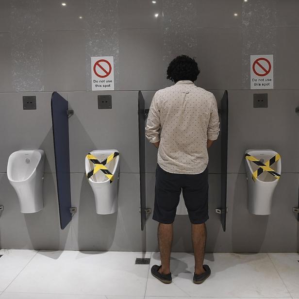 Ein Mann steht in einer öffentlichen Toilette vor einem Urinal, während andere mit Warnband abgesperrt sind.