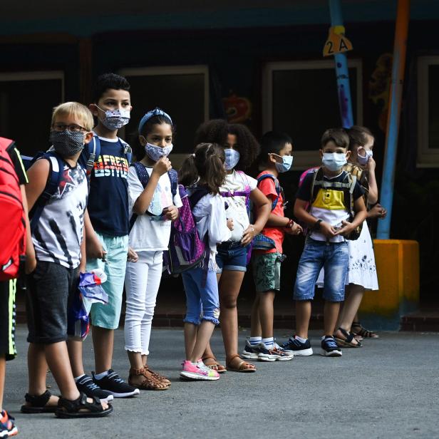 Eine Gruppe von Schulkindern steht mit Masken vor einem Gebäude.