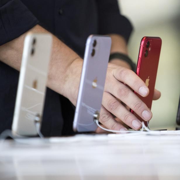 Eine Hand berührt ein rotes iPhone, das neben anderen iPhones in verschiedenen Farben steht.