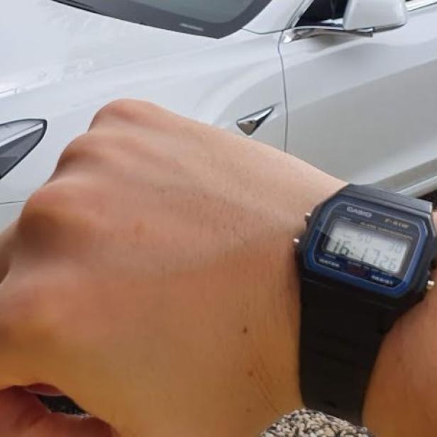 Eine Person trägt eine Casio-Digitaluhr vor einem weißen Tesla.
