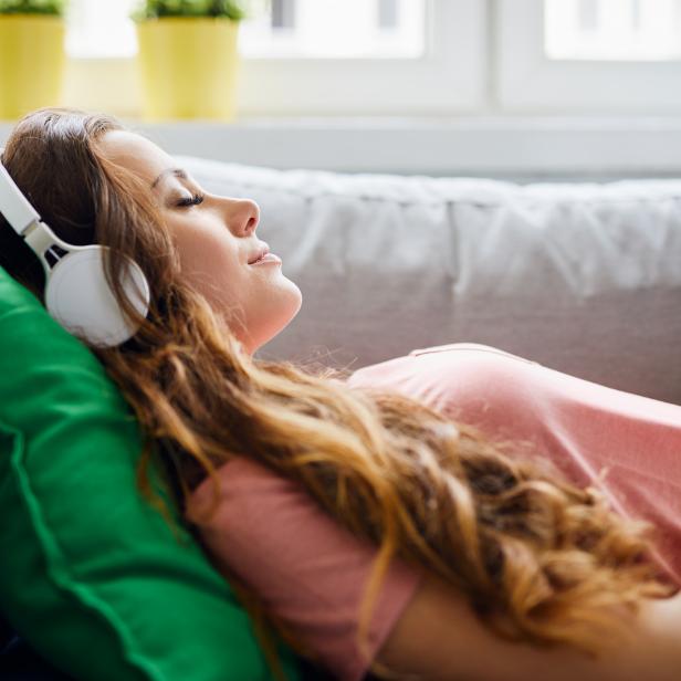 Portrait of a beautiful young woman lying on sofa with headphones on and closed eyes, relaxing