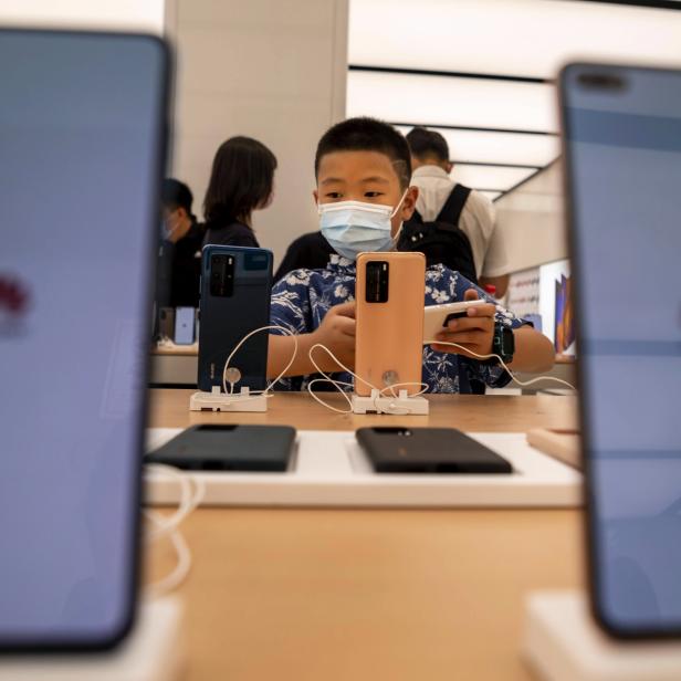 Ein Junge mit Maske spielt in einem Huawei-Store in Shanghai mit einem Smartphone.