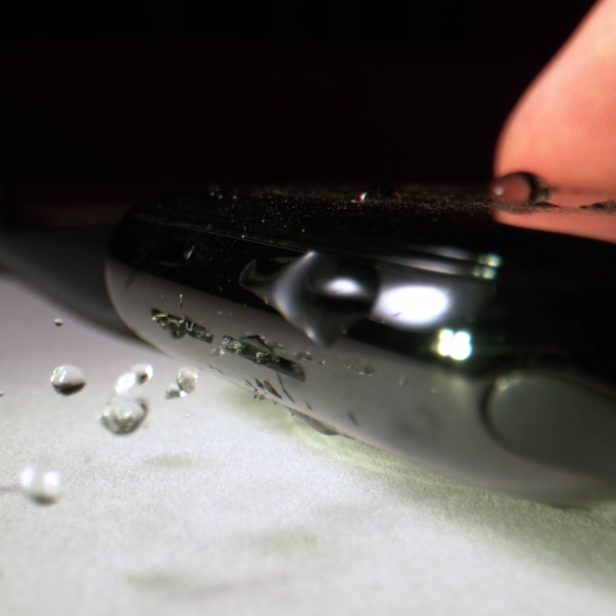 Ein Finger berührt eine Smartwatch, auf der sich Wassertropfen befinden.