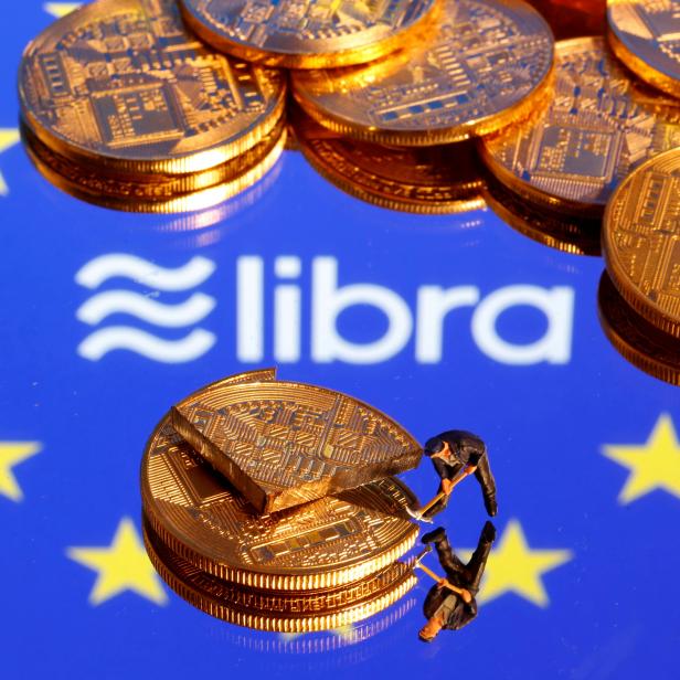 FILE PHOTO: A small toy figure is seen on representations of the virtual currency on a displayed European Union flag and the Facebook Libra logo in this illustration picture