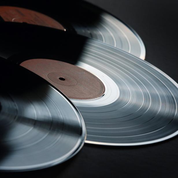 Drei Schallplatten liegen übereinander auf einer dunklen Oberfläche.