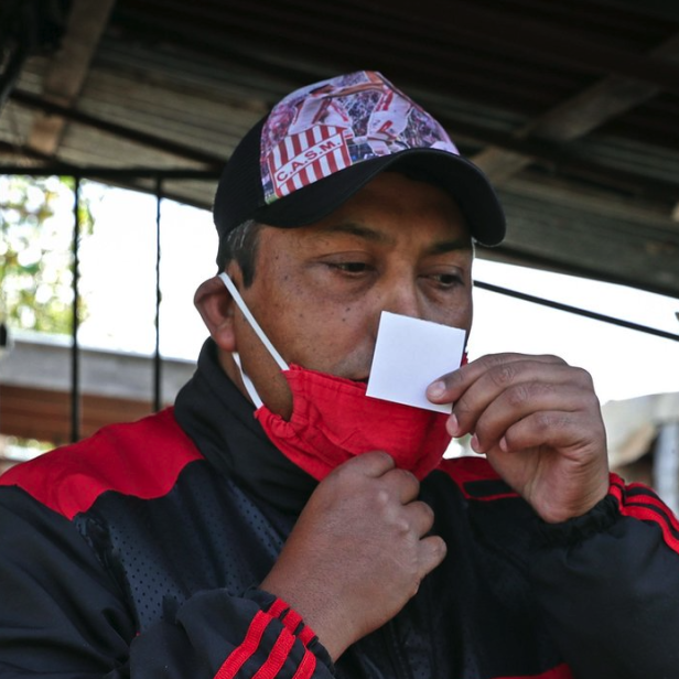 Ein Mann mit Maske hält einen kleinen Zettel vor seine Nase.