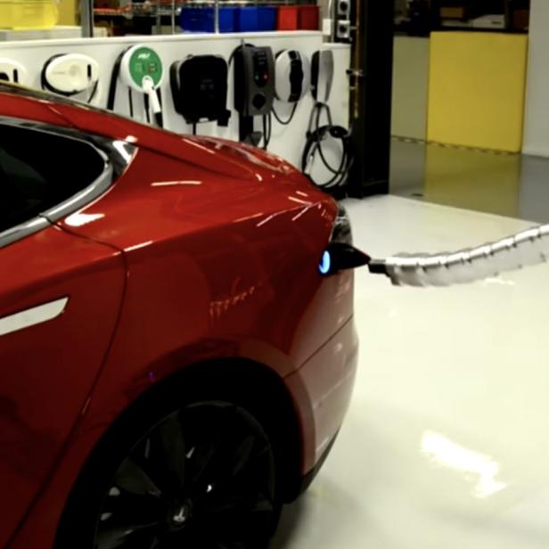 Ein rotes Tesla-Auto wird von einem Roboterarm aufgeladen.