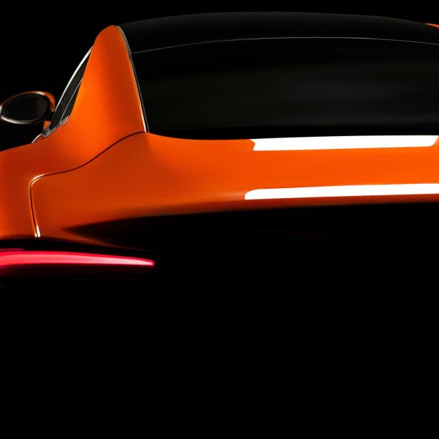Die Rückansicht eines orangefarbenen Autos mit schwarzem Dach vor dunklem Hintergrund.