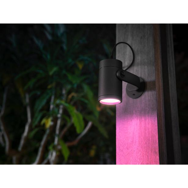 Eine schwarze Außenleuchte strahlt rosa Licht auf einen Holzpfosten.