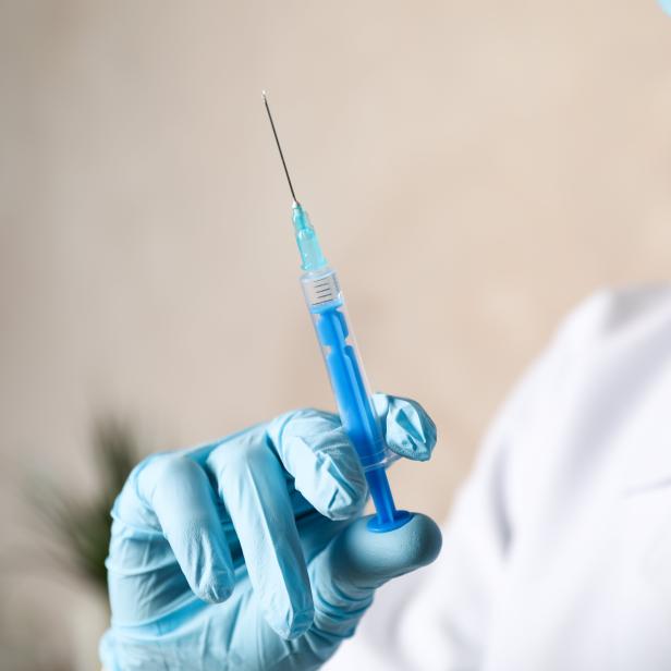 Doctor holds medical syringe of vaccine, injection on brown background. Coronavirus protection. Healthcare and medical concept