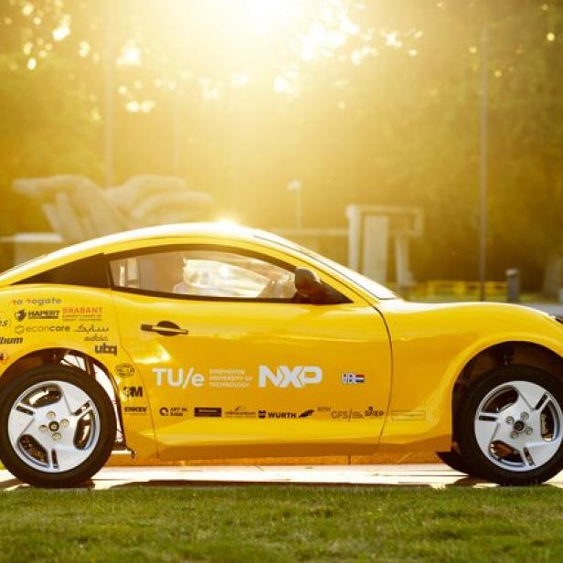 Ein gelbes Auto der TU Eindhoven steht im goldenen Gegenlicht auf einer Wiese.