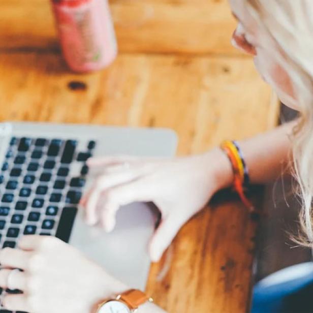 Eine Frau mit blonden Haaren arbeitet an einem Laptop an einem Holztisch.