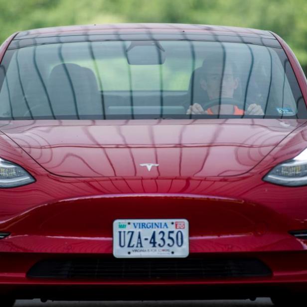 Ein rotes Tesla Model 3 fährt auf einer Straße.