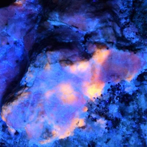Ein Mineral leuchtet unter ultraviolettem Licht in Blau und Orange.
