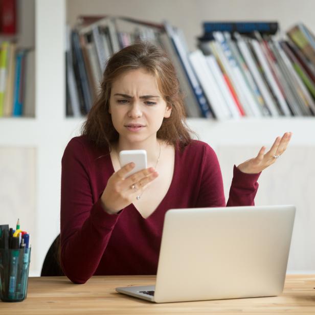 Frustrated female entrepreneur looking at cellphone and shrugging.