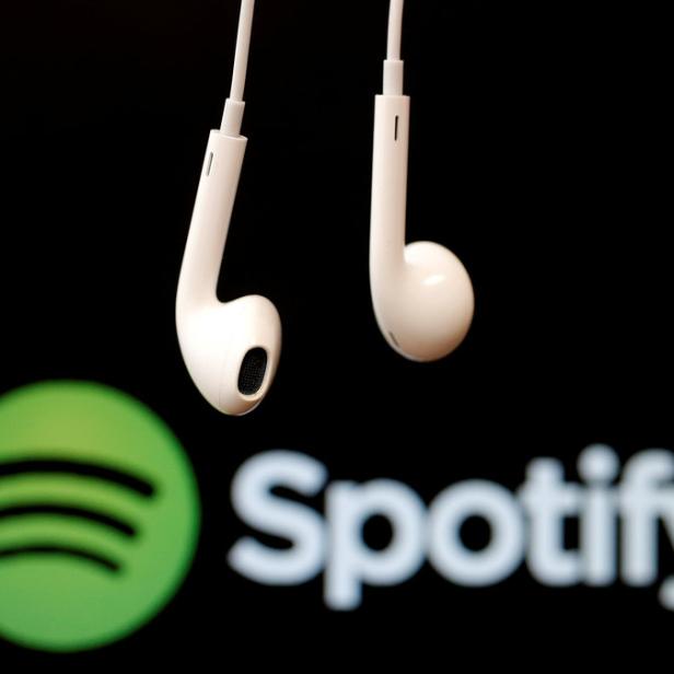 Weiße Kopfhörer hängen vor dem Spotify-Logo.