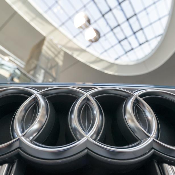 Das Audi-Logo auf einem Kühlergrill vor einem modernen Gebäude.