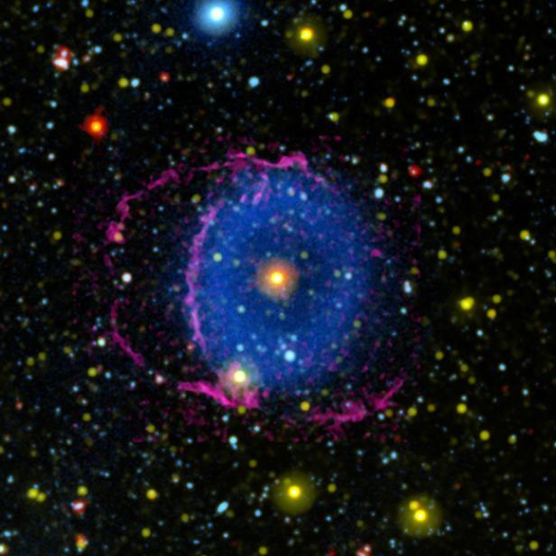 Ein blauer planetarischer Nebel umgeben von einem rosa Ring und vielen Sternen.