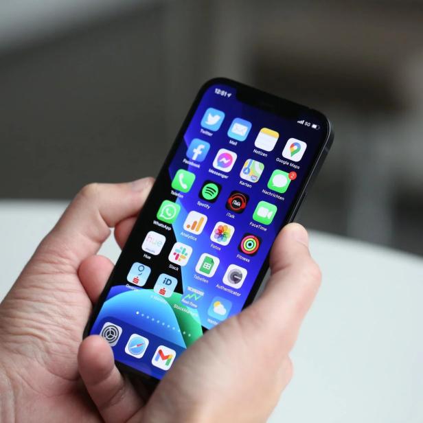 Eine Person hält ein iPhone mit verschiedenen App-Symbolen auf dem Bildschirm.