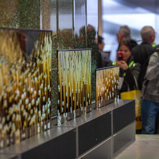Mehrere transparente Fernsehbildschirme zeigen abstrakte Kunst auf einer Messe.