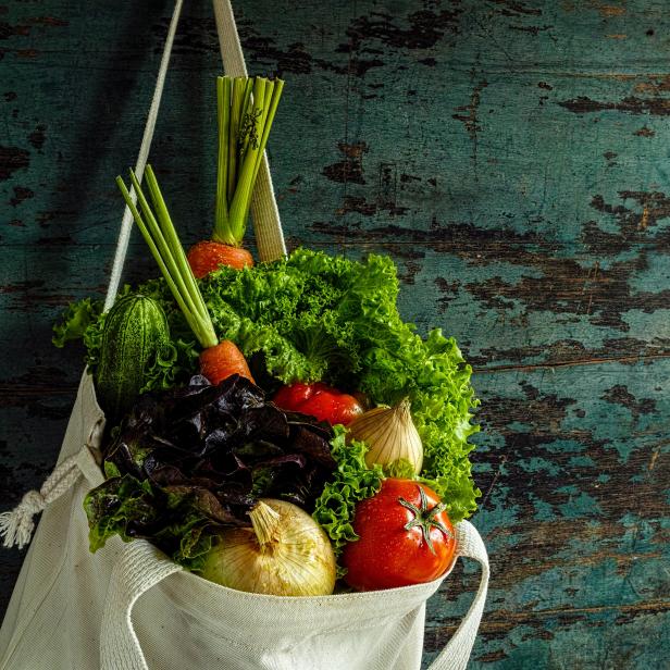 Market fresh salad vegetables hanging in a natural cotton recyclable shopping bag by a hook on a wooden turquoise coloured wall.