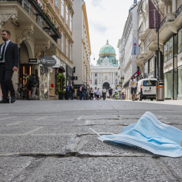 Eine weggeworfene Maske auf der Straße in Wien, im Hintergrund die Hofburg.