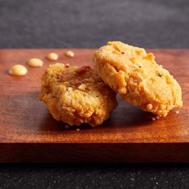 Zwei goldbraune Chicken Nuggets liegen auf einem Holzbrettchen.