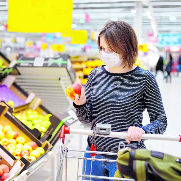 Junge Frau mit medizinischer Maske kauft während des Coronavirus-Ausbruchs im Supermarkt ein.