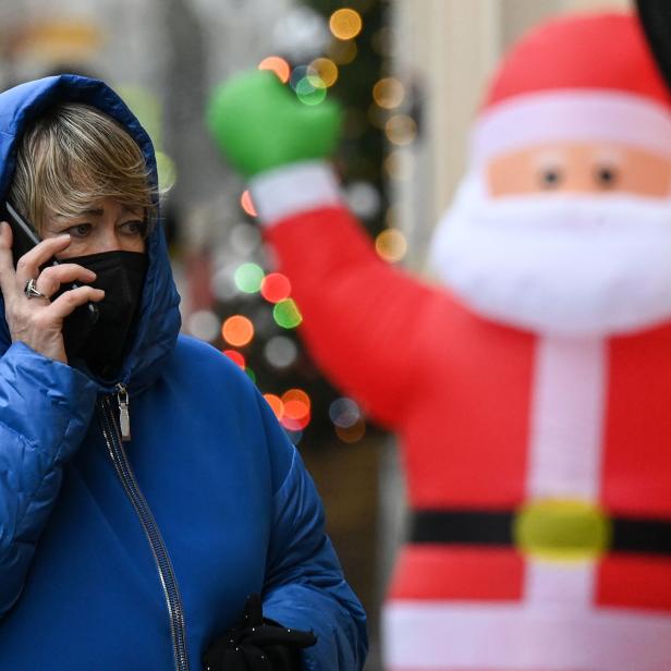 Eine Frau mit Maske telefoniert vor einer Weihnachtsdekoration.