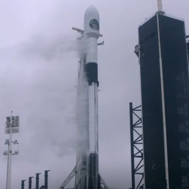 Eine Falcon 9 Rakete steht auf einer Startrampe neben einem Turm.