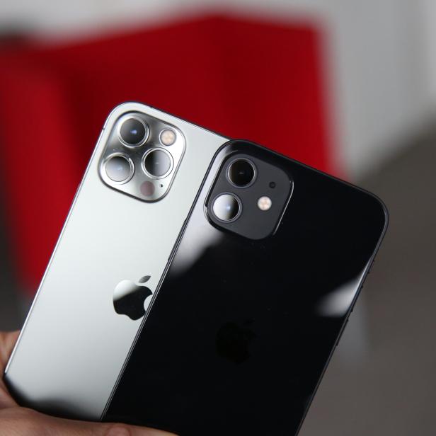Eine Hand hält ein silbernes und ein schwarzes iPhone.