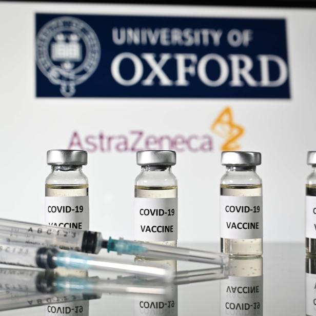Mehrere Fläschchen des COVID-19-Impfstoffs von AstraZeneca vor dem Logo der Universität Oxford.