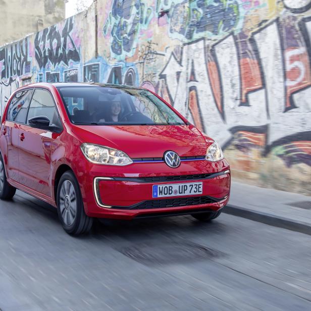 Ein roter VW e-up! fährt vor einer Wand mit Graffiti.