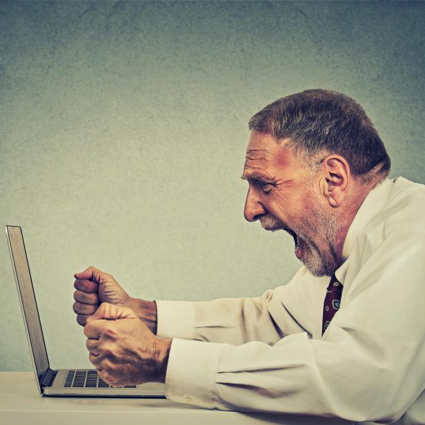 Angry senior business man working on computer screaming